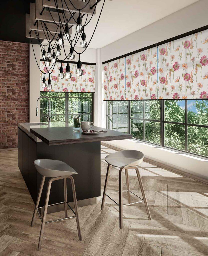 Floral print roller blinds across a long run of kitchen windows behind an island with bar stools