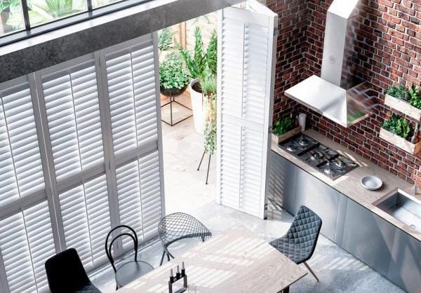 White shutters on tall windows in a kitchen-diner seen from above, with a hob and extractor on a brick wall