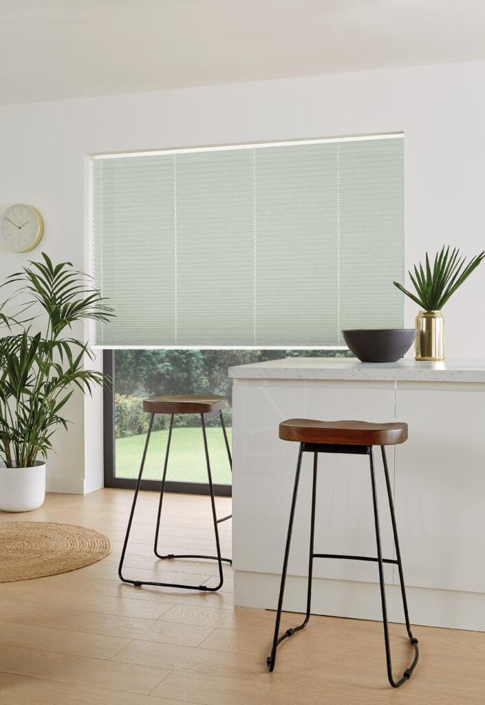 Pale green pleated blind on a wide window beside a white kitchen island and two stools