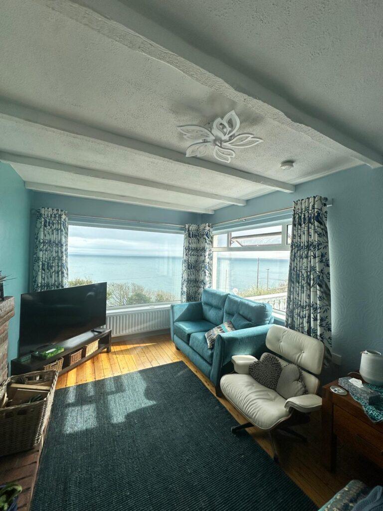 Blue and white patterned curtains framing wide windows that look out to sea in a living room