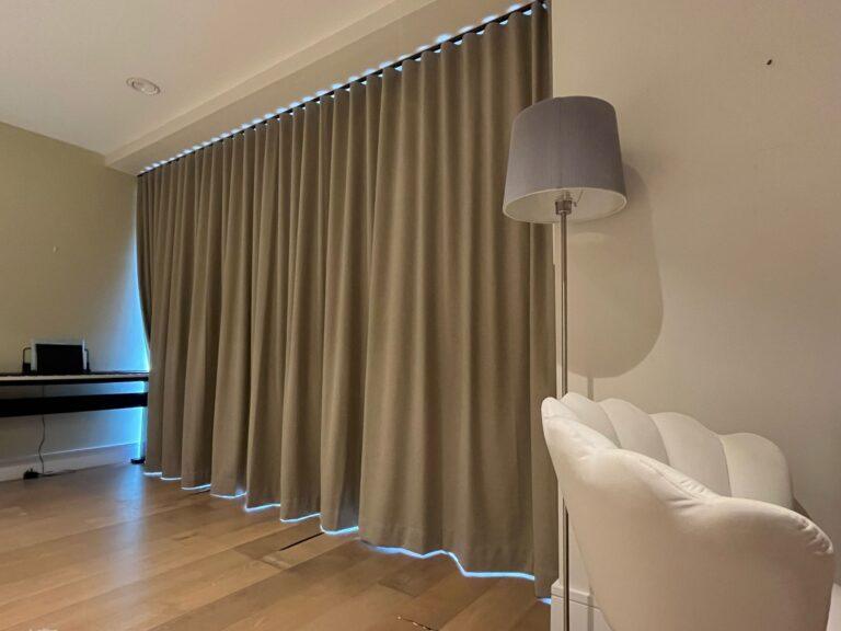Taupe wave heading curtains running the full length of a wall, lit by a strip light above and below