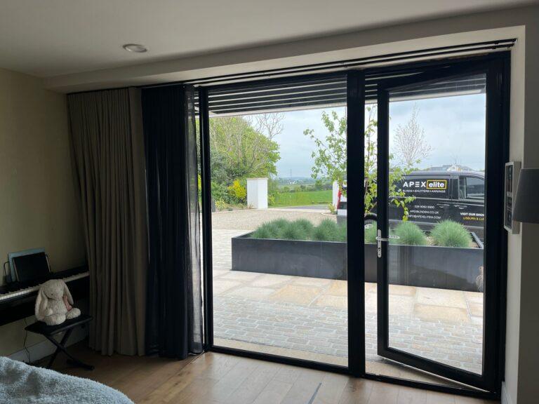 Taupe floor-length curtains and a dark sheer drawn back from black glazed doors that open onto a patio
