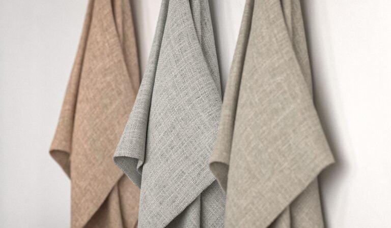 Three lengths of textured curtain fabric in terracotta, grey and natural linen hanging against a white wall